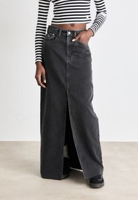 Črna jeans maks krila s sprednjim razporkom, petimi žepi in gumbom za zapiranje. Ujemajoče se z dolgem rokavom s črno-belimi črtami.