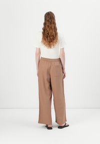 Lys beige t-skjorte i kombinasjon med løstsittende, brune linbukser med elastisk midje og en enkel baklomme.