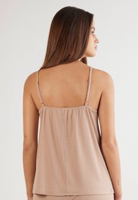 Beige geribbelde tanktop met verstelbare spaghetti schouderbandjes. Bevat gerimpelde details aan de achterkant en heeft een losse pasvorm. Glad materiaal.