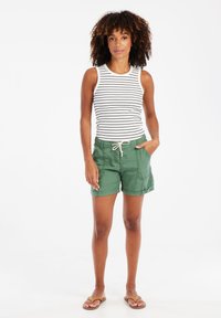 Gestreepte mouwloze top en groene shorts met trekkoord; de shorts hebben zijzakken en opgerolde cuffs; gedragen met platte sandalen.