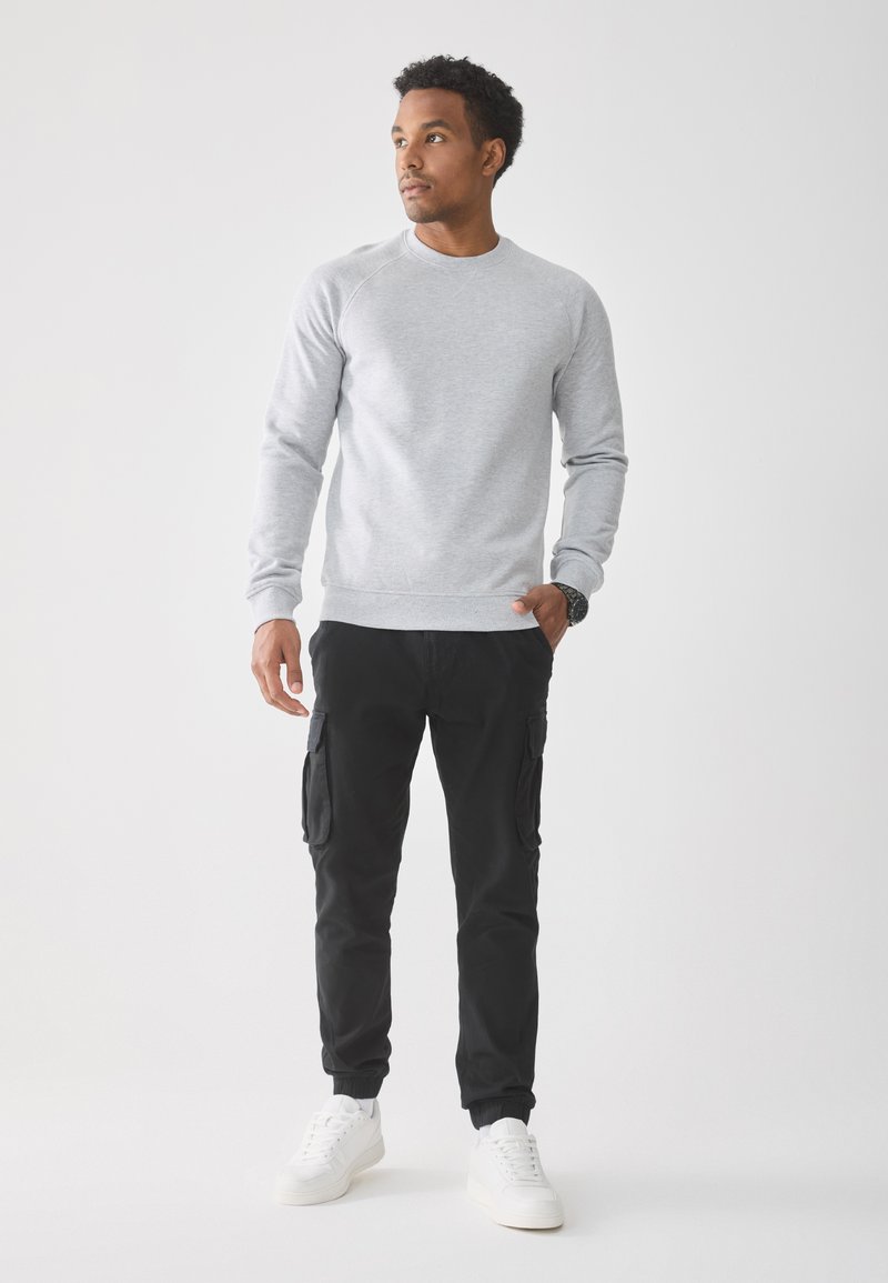 Grijze sweatshirt met ronde hals en geribde manchetten, gecombineerd met zwarte cargobroek met zijzakken en witte sneakers.