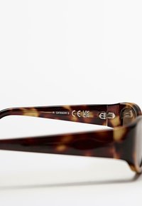 Occhiali da sole tartarugati marroni con montatura spessa, dettagli in metallo argentato e informazioni di certificazione stampate sulla tempia interna destra.
