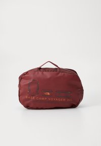 Sac en nylon rouge avec une anse, présentant des dessins techniques en orange, étiqueté "BASE CAMP VOYAGER 32L", mettant en avant les compartiments de rangement.