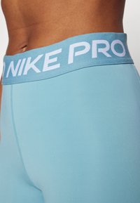 Zbliżenie na osobę w jasnoniebieskich legginsach Nike Pro, pokazujące pas oraz część odkrytej torsu.