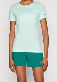 Jasnozielona bawełniana koszulka z okrągłym dekoltem i krótkimi rękawami, zestawiona z turkusowymi bawełnianymi szortami z logo na brzegu.