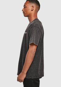 Camiseta de algodón negra de manga corta y corte holgado, con textura desgastada y lettering discreto en la parte delantera, con un cuello redondo y un ajuste relajado.