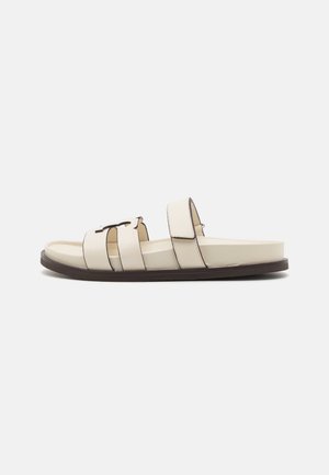 Chanclas de piel color beige claro con tres tiras anchas, un acabado de cuero suave y una suela marrón texturizada baja. Diseño minimalista sin hardware visible.