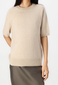 Pull beige à manches courtes en maille douce avec un col rond et un ourlet côtelé. Associé à une jupe lisse couleur olive foncé.