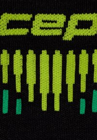 Schwarzer Strickstoff mit auffälliger grüner Schrift und Mustern. Das Design umfasst abstrakte Formen mit türkisfarbenen Akzenten.