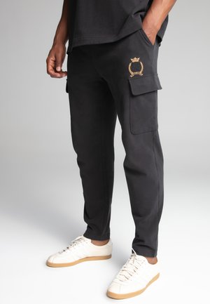 Svarta cargo-byxor i bomull, med en sidoficka, guld-embroderad logotyp och en avsmalnande ben-design. Kombinerade med vita sneakers.