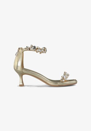 Złote metaliczne sandały na obcasie z wąskim noskiem, z kryształową ozdobną regulacją w kostce i szerokim paskiem z przodu, z niskim obcasem w kształcie bloku.