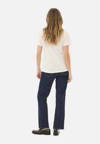 T-shirt bianco a maniche corte con orlo arrotondato, abbinato a jeans a gamba dritta blu scuro. Presenta tasche posteriori e mocassini neri lucidi e lisci.
