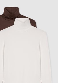 Due maglie a manica lunga con colletto alto, una bianca davanti e una marrone parzialmente visibile dietro, su uno sfondo chiaro e semplice.