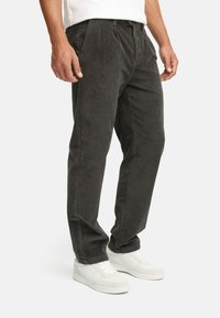 Dark grey corduroy pants with a pleated front, tapered legs, and a textured finish, paired with white sneakers.