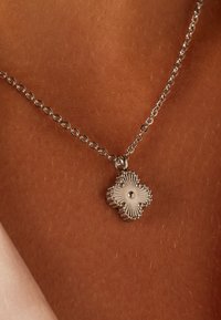 Zilveren halsketting met een bloemvormige hanger, voorzien van gestructureerde ribbels en een centrale kraal. De schakels van de ketting zijn rond en glad.