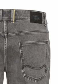 Gray denim jeans feature a logoed black patch at the waistband, yellow stitching, and two back pockets with curved seams.