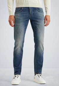 Jeans de mezclilla azul deslavado con corte ajustado, diseño de cinco bolsillos y ligeras marcas de desgaste. Combinados con zapatillas blancas con detalles negros.