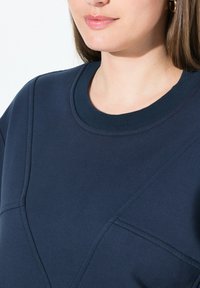 Felpa blu navy con collo rotondo, cuciture testurizzate e vestibilità comoda con dettagli di cuciture diagonali. Finitura in tessuto liscia.