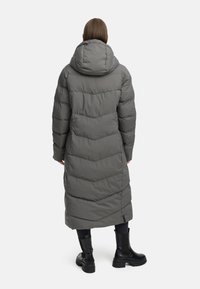 Lang grå pufferfrakke med chevron-syninger, hætte og lige snit, parret med sorte knæhøje støvler. Glat tekstur hele vejen igennem.