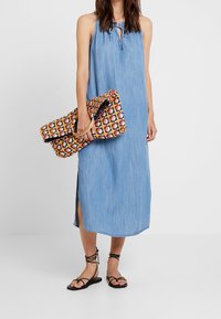 Denim halterklänning med knytkrage, sidöppning och avslappnad passform. Matchad med en färgglad mönstrad clutch och svarta sandaler med remmar.