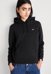 Sudadera negra hecha de material suave, con un bolsillo canguro frontal, capucha con cordón y un pequeño logotipo en el pecho.
