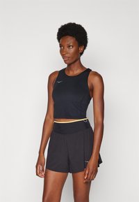 Svart crop top med rund halsringning och axelband, tillsammans med svarta shorts med ribbad midja och guldaccenter. Enkel design.