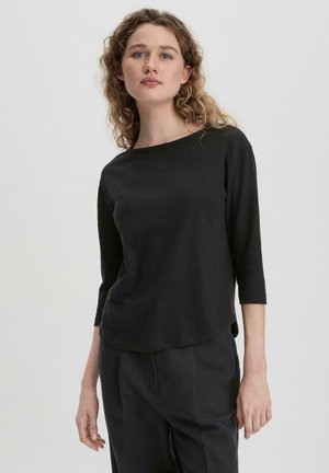 Haut noir à manches longues avec encolure large et ourlet arrondi, fabriqué en tissu doux, associé à un pantalon noir ample avec un design simple.