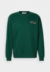 Sweatshirt vert foncé avec un col rond, des manches longues et des poignets côtelés. Arbore l'inscription "Lazy Morning Brew Society" brodée en orange et blanc.