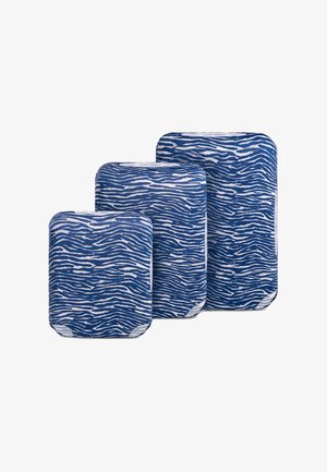 Trzy niebiesko-białe pokrowce na bagaż w paski zebry, w rozmiarach: mały, średni i duży, ułożone obok siebie na białym tle.