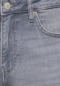 Κοντινό πλάνο γκρι τζιν υφάσματος δείχνοντας την μπροστινή τσέπη, το θηλάκι της ζώνης και ένα μεταλλικό κουμπί με την επιγραφή «ONLY & SONS».