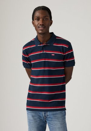 Mørkeblå stribet polo t-shirt med røde og hvide striber, med krave og tre-knaps placket. Logo-patch på venstre bryst.