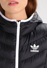 Černá péřová bunda s bílým zipem a kapucí, s diagonálním prošíváním a bílým logem Adidas na levé straně.