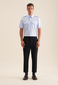 Camicetta azzurra chiara a maniche corte con due tasche frontali, abbinata a pantaloni neri su misura e scarpe nere. Design semplice con una vestibilità pulita.