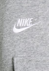 Grå sweatshirt i mjukt material, med en vit broderad Nike-logga och texturerat tyg, med en enkel och avskalad design.