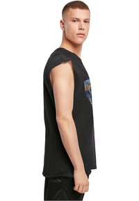 Melna bez piedurknēm T-kreklu, kas izgatavots no kokvilnas, ar grafisku dizainu priekšpusē un neapstrādātām malām, lai radītu nolietotu izskatu.