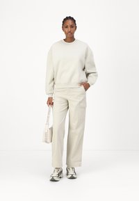 Helles beige Sweatshirt mit übergroßem Schnitt und gerippten Bündchen. Passende beiges Cargo-Hose mit Taschen, kombiniert mit gemusterten Sneakers und Tasche.