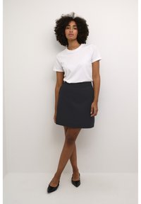 T-shirt blanc à manches courtes associé à une jupe noire en A. La tenue est simple, avec des lignes épurées et une silhouette ajustée.