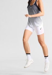 Camiseta deportiva de rayas azules marino y blancas con espalda nadadora, combinada con pantalones cortos blancos. Cuenta con el logo negro de Nike y zapatillas blancas con suelas grises.