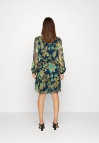 Šaty s květinovým potiskem na tmavě modrém pozadí, průsvitné dlouhé rukávy, nařasený pas a volánkový lem. Celkový vzhled doplňují černé sandály na podpatku.