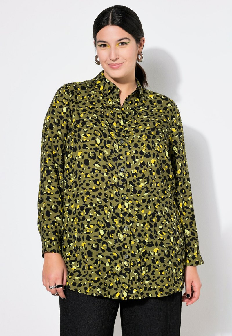 Camisa de botón con estampado de leopardo verde y acentos en negro y amarillo, con cuello y mangas largas, combinada con pantalones negros texturizados.