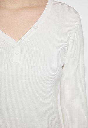 Witte geribbelde lange mouw top met een V-hals en drie knopen bij de halslijn, met een soepele textuur en een getailleerd ontwerp.