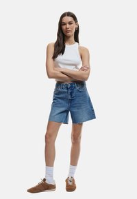 Farkkuhousut, joissa on hapsureunat, korkea vyötärö ja sivutaskut, yhdistetty valkoiseen ribbipintaiseen toppiin ja ruskeisiin urheilukenkihin.