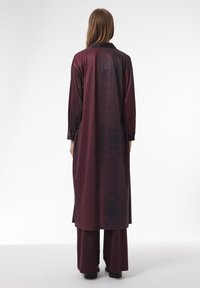 Lang bordeauxrood jurk met een gestructureerd krokodillenpatroon, voorzien van een kraag, lange mouwen en zijslitsen, gecombineerd met bijpassende broeken.