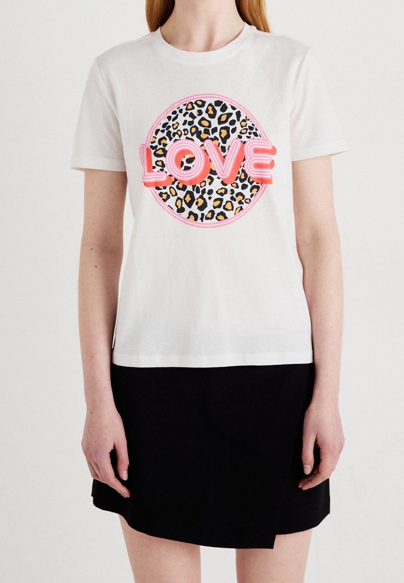 T-shirt blanc à manches courtes en coton, avec un imprimé rond léopard et le mot "LOVE" en texte rose néon.