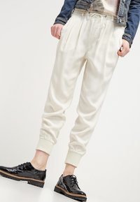 Krämliknande satin joggerbyxor med dragsko i midjan och elastiska muddar. Kombinerat med blanka svarta snörskor och en denimjacka.