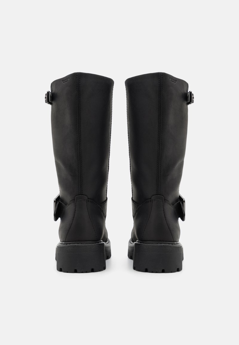 Ein Paar hohe schwarze Lederstiefel mit dicken Sohlen und seitlichen Schnallen, von hinten auf einem weißen Hintergrund gezeigt.