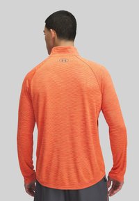 Langärmliges Sportshirt in leuchtendem Orange, mit strukturiertem Muster, hohem Kragen und einem Logo auf der Rückseite. Glatter, leichter Stoff.