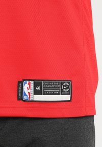 Červený NBA dres s síťovanou texturou. Obsahuje velikostní štítek (48) a značení Nike. Zahrnuje černý štítek s podrobnostmi o autentičnosti.