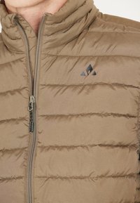Beige gewatteerd vest met een hoge kraag, voorzien van horizontaal gestikte secties, een ritsluiting en een klein zwart logo op de borst.