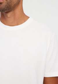 White cotton crew-neck t-shirt with short sleeves. Smooth texture and minimal design. Close-up view showing neckline and shoulder.